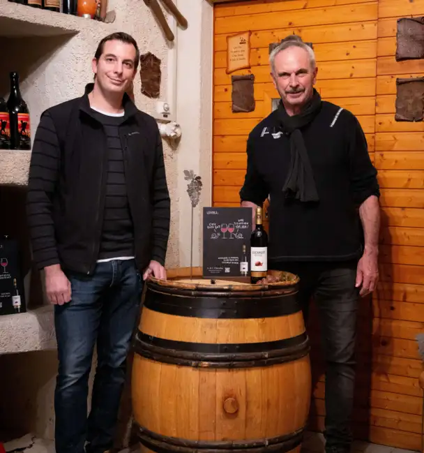 Andr&eacute; et Christophe Chevalley dans leur cave, pr&eacute;sentant la bouteille "Escargot rouge" pos&eacute;e sur un tonneau.
